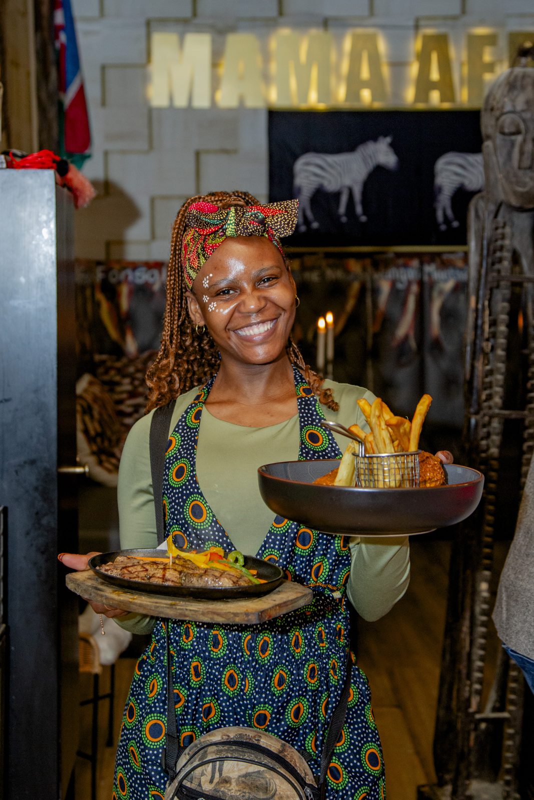 A Mama Africa host carrying plates of African food